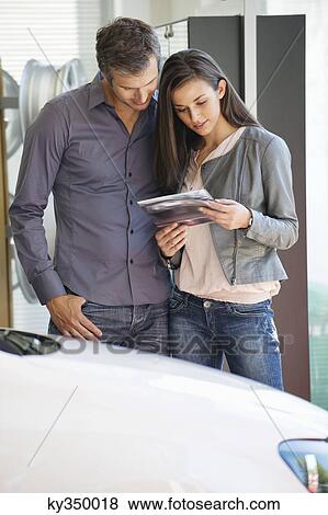 Happy couple looking at car catalog in showroom View Large Photo Image Stock Photo - Happy couple looking at car catalog in showroom. Fotosearch