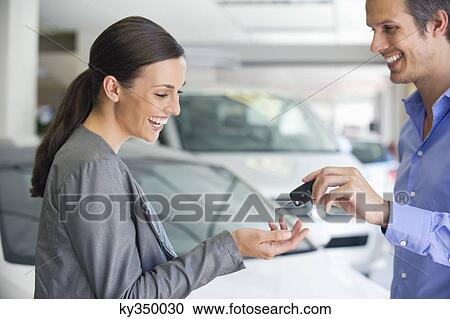 Happy salesperson handing car key to a woman in a showroom View Large Photo Image Stock Image - Happy salesperson handing car key to a woman in a showroom. Fotosearch