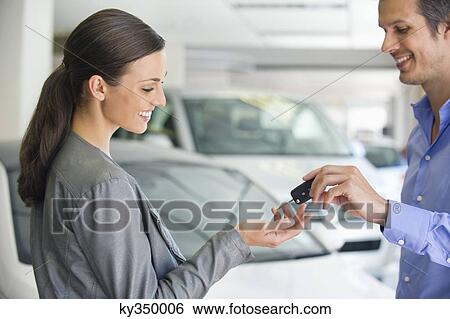 Happy salesperson handing woman car key in showroom View Large Photo Image Stock Photograph - Happy salesperson handing woman car key in showroom. Fotosearch