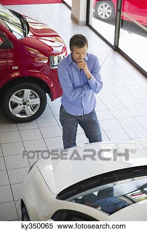Stock Photography - Mid adult man looking at a car in a showroom. Fotosearch