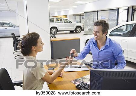 Saleswoman handling car key to a man View Large Photo Image Stock Photo - Saleswoman handling car key to a man. Fotosearch