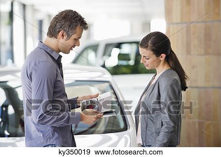 Side profile of a couple looking at catalog in car showroom View Large Photo Image Stock Photo - Side profile of a couple looking at catalog in car showroom. Fotosearch