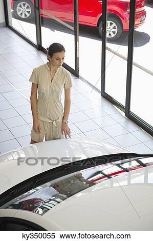 Young woman looking at a car in a showroom View Large Photo Image Stock Photography - Young woman looking at a car in a showroom. Fotosearch