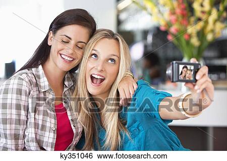 Stock Photograph - Female friends taking a picture of themselves with a camera. Fotosearch