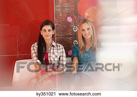 Portrait of female friends sitting on a sofa in a cafe View Large Photo Image Stock Image - Portrait of female friends sitting on a sofa in a cafe. Fotosearch