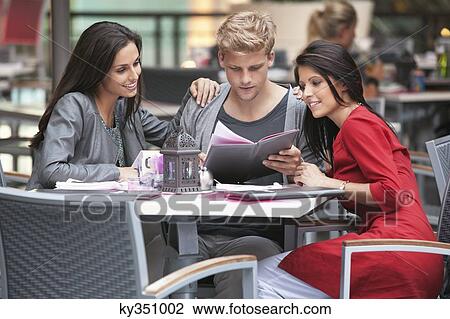 Young man with two young women looking at menu in a restaurant View Large Photo Image Stock Image - Young man with two young women looking at menu in a restaurant. Fotosearch