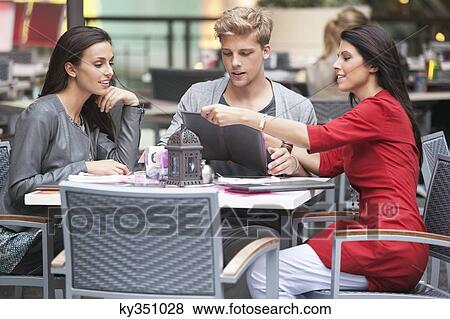 Young man with two young women looking at menu in a restaurant View Large Photo Image Stock Photo - Young man with two young women looking at menu in a restaurant. Fotosearch