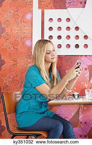 Young woman sitting in a cafe and text messaging on a mobile phone View Large Photo Image Stock Image - Young woman sitting in a cafe and text messaging on a mobile phone. Fotosearch
