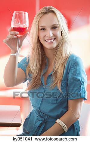 Young woman toasting wine glass and smiling in a bar View Large Photo Image Stock Image - Young woman toasting wine glass and smiling in a bar. Fotosearch