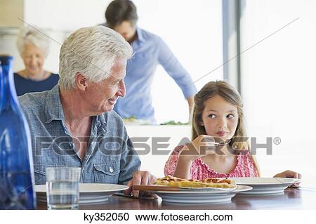 Girl eating food at a dining table with her grandfather sitting near her View Large Photo Image Stock Image - Girl eating food at a dining table with her grandfather sitting near her. Fotosearch