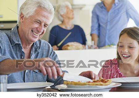 Stock Image - Man cutting cake with a knife and his granddaughter sitting near him. Fotosearch