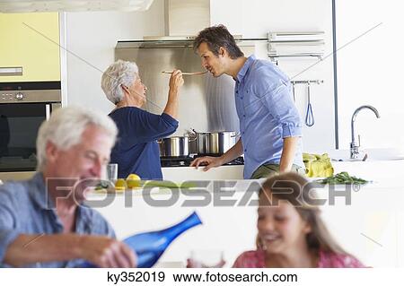 Stock Photo - Man pouring water into a glass while his wife feeding food to her son. Fotosearch