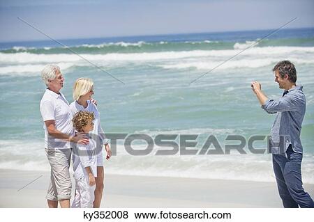 Stock Photo - Mid adult man taking picture of his family on the beach. Fotosearch
