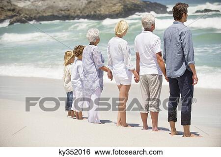 Stock Photograph - Rear view of a multi generation family standing on the beach. Fotosearch