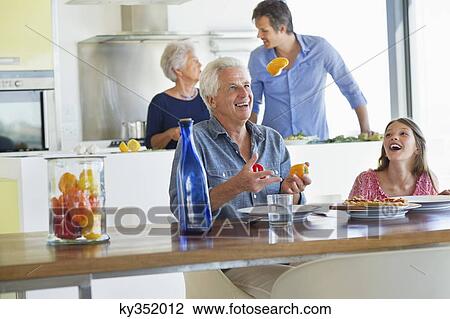 Stock Image - Senior man smiling with his granddaughter at a dining table. Fotosearch