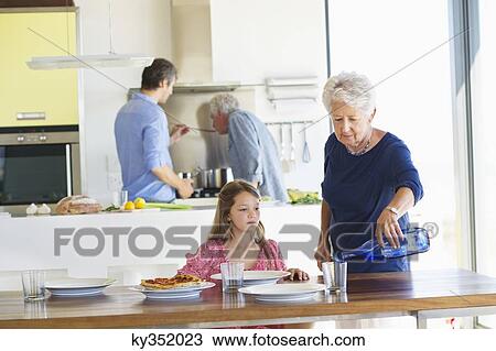Stock Image - Senior woman pouring water into a glass at a dining table. Fotosearch