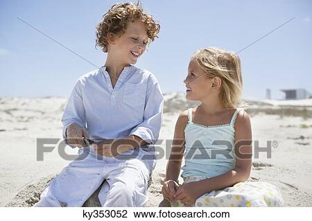 Boy with his sister sitting on the beach and smiling View Large Photo Image Stock Image - Boy with his sister sitting on the beach and smiling. Fotosearch