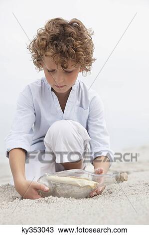 Cute boy looking at message in a bottle on beach View Large Photo Image Stock Image - Cute boy looking at message in a bottle on beach. Fotosearch