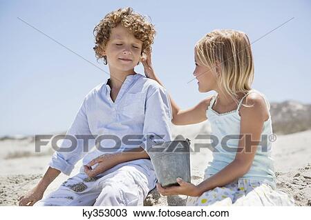 Girl holding shell to her brother's ear on beach View Large Photo Image Stock Image - Girl holding shell to her brother's ear on beach. Fotosearch
