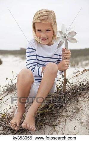 Portrait of a smiling girl sitting on sand and holding pinwheel View Large Photo Image Stock Photography - Portrait of a smiling girl sitting on sand and holding pinwheel. Fotosearch
