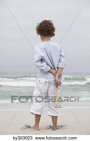 Rear view of a boy holding bottle with message on the beach View Large Photo Image Stock Image - Rear view of a boy holding bottle with message on the beach. Fotosearch