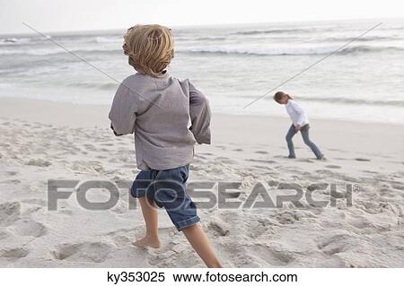 Stock Photography - Rear view of a boy running on the beach with his sister. Fotosearch