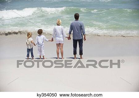 Stock Image - Couple with two children standing on the beach. Fotosearch