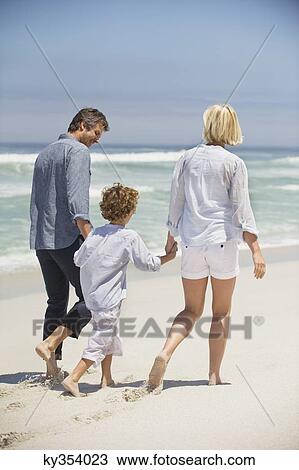 Stock Image - Rear view of a couple walking with their son on the beach. Fotosearch