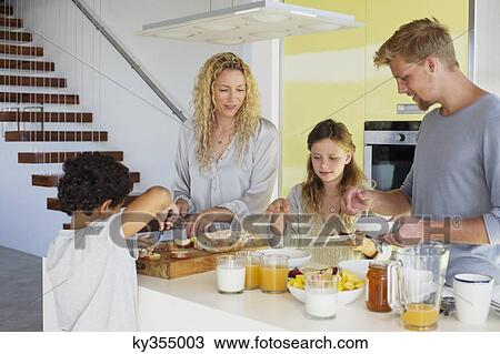 Stock Image - Couple with their two children preparing food at a domestic kitchen. Fotosearch