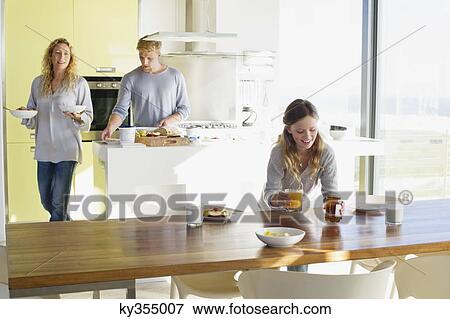 Girl putting breakfast on a dining table with her parents in the background View Large Photo Image Stock Photo - Girl putting breakfast on a dining table with her parents in the background. Fotosearch