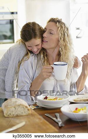Stock Photography - Mid adult woman kissing her daughter at a dining table. Fotosearch