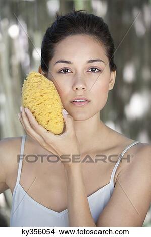 Beautiful young woman holding a bath sponge on her face View Large Photo Image Picture - Beautiful young woman holding a bath sponge on her face. Fotosearch