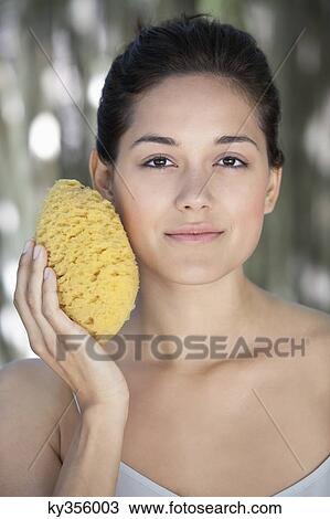 Beautiful young woman holding a bath sponge on her face View Large Photo Image Stock Image - Beautiful young woman holding a bath sponge on her face. Fotosearch