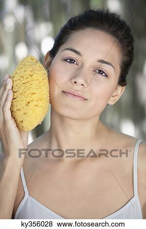 Beautiful young woman holding a bath sponge on her face View Large Photo Image Stock Photo - Beautiful young woman holding a bath sponge on her face. Fotosearch