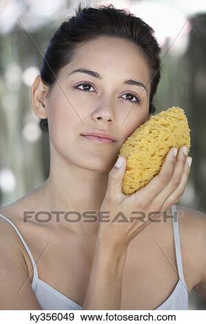 Beautiful young woman holding a bath sponge on her face View Large Photo Image Stock Photo - Beautiful young woman holding a bath sponge on her face. Fotosearch