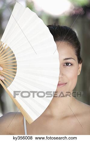 Beautiful young woman holding a Chinese fan in front of her face View Large Photo Image Stock Photo - Beautiful young woman holding a Chinese fan in front of her face. Fotosearch