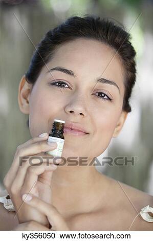 Stock Image - Portrait of a beautiful young woman smelling aromatherapy oil. Fotosearch