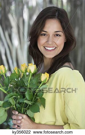 Portrait of a young woman holding bunch of yellow flowers View Large Photo Image Stock Image - Portrait of a young woman holding bunch of yellow flowers. Fotosearch