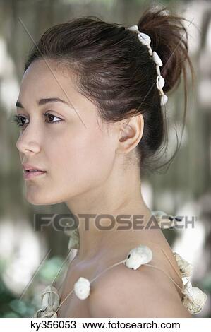 Stock Image - Side profile of a beautiful young woman wearing a shell necklace. Fotosearch