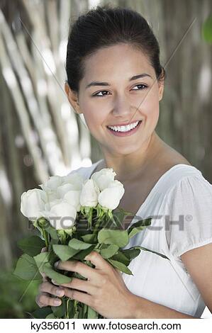 Stock Image - Young woman holding bunch of white flowers and smiling. Fotosearch