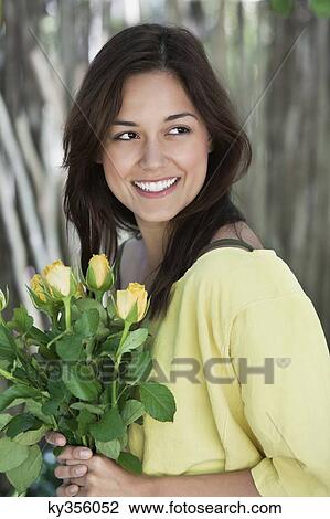Stock Image - Young woman holding bunch of yellow flowers and smiling. Fotosearch