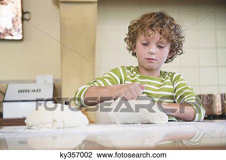 Stock Image - Cute little boy kneading dough at kitchen. Fotosearch