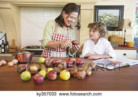 Stock Image - Grandmother and little boy peeling fruit at home. Fotosearch