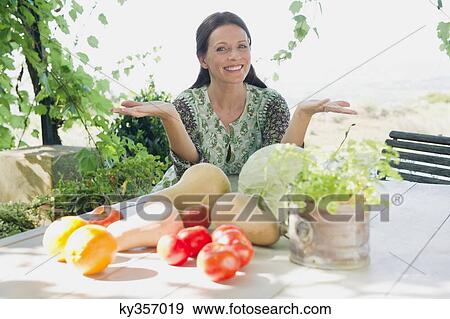 Portrait of a mature woman sitting with vegetables on table View Large Photo Image Stock Photo - Portrait of a mature woman sitting with vegetables on table. Fotosearch