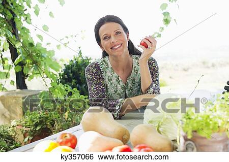 Portrait of a mature woman sitting with vegetables on table View Large Photo Image Stock Photograph - Portrait of a mature woman sitting with vegetables on table. Fotosearch