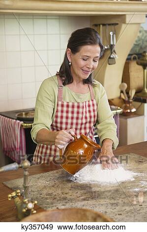 Smiling senior woman pouring water in flour View Large Photo Image Stock Photo - Smiling senior woman pouring water in flour. Fotosearch