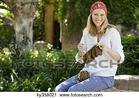 Stock Image - Cheerful young woman knitting. Fotosearch