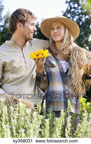 Stock Image - Young couple in scarecrow pose in a field. Fotosearch