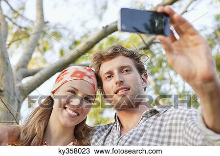 Young couple taking a picture of themselves with a mobile phone View Large Photo Image Stock Image - Young couple taking a picture of themselves with a mobile phone. Fotosearch