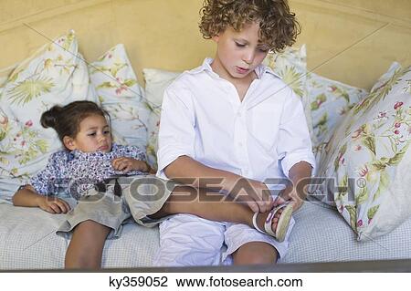 Stock Image - Boy putting sandal to her sister. Fotosearch
